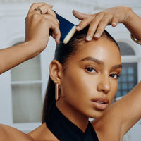 Model applying Oribe Supershine Smoothing Wax Stick at the hairline