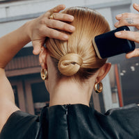 Oribe Supershine Smoothing Wax Stick being applied to a bun